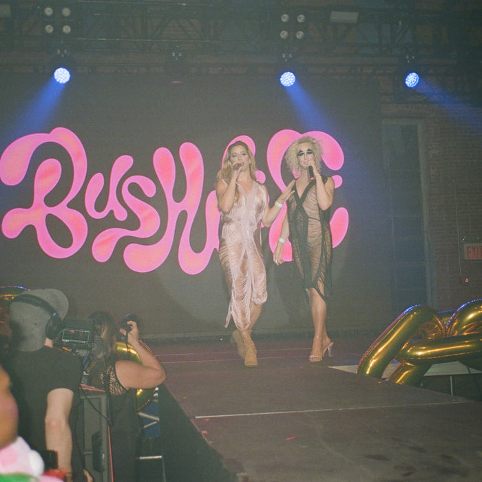 hosts on stage in front of bushwig sign. 