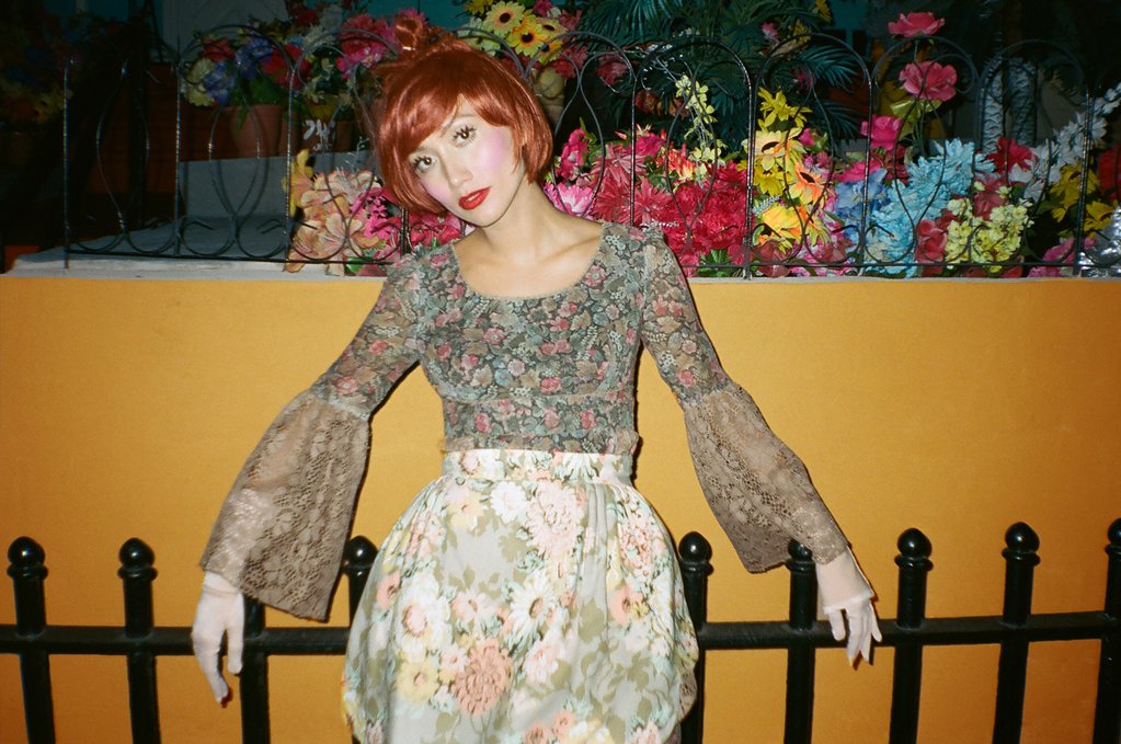 model posing againt fence with fake flowers in background.