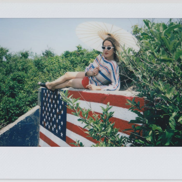 model with paper umbrella in red white and blue lying on top of an american flag.