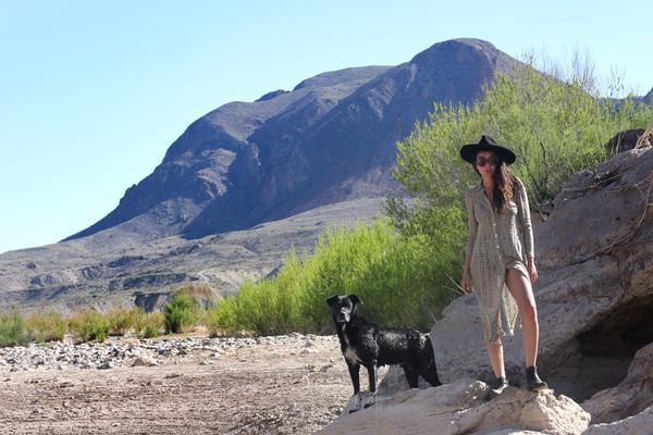 aisha standing on a rock with a black dog, and a mountain in the background.