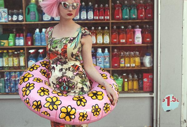 zuzu in gorgeous dress with ring pool float in front of a bodega.