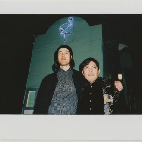 employees posing, neon flamingo bar entrance behind - polaroid style.