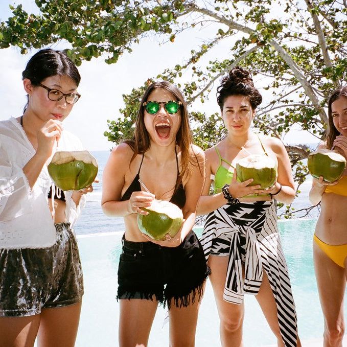 people drinking coconuts in front of a pool and ocean in the background.