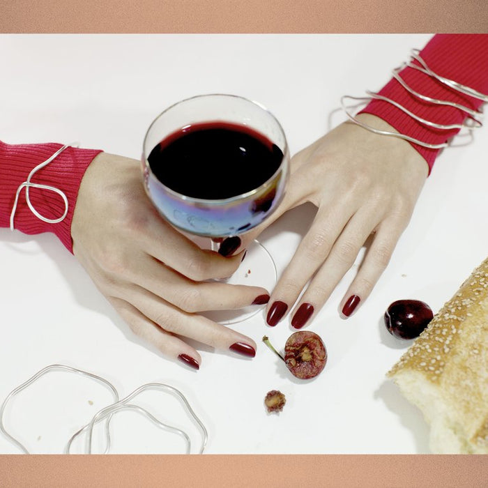 still life of hands in bracelets with glass of wine and cherries.