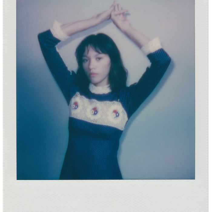polaroid of model posing in a dress with arms above their head.