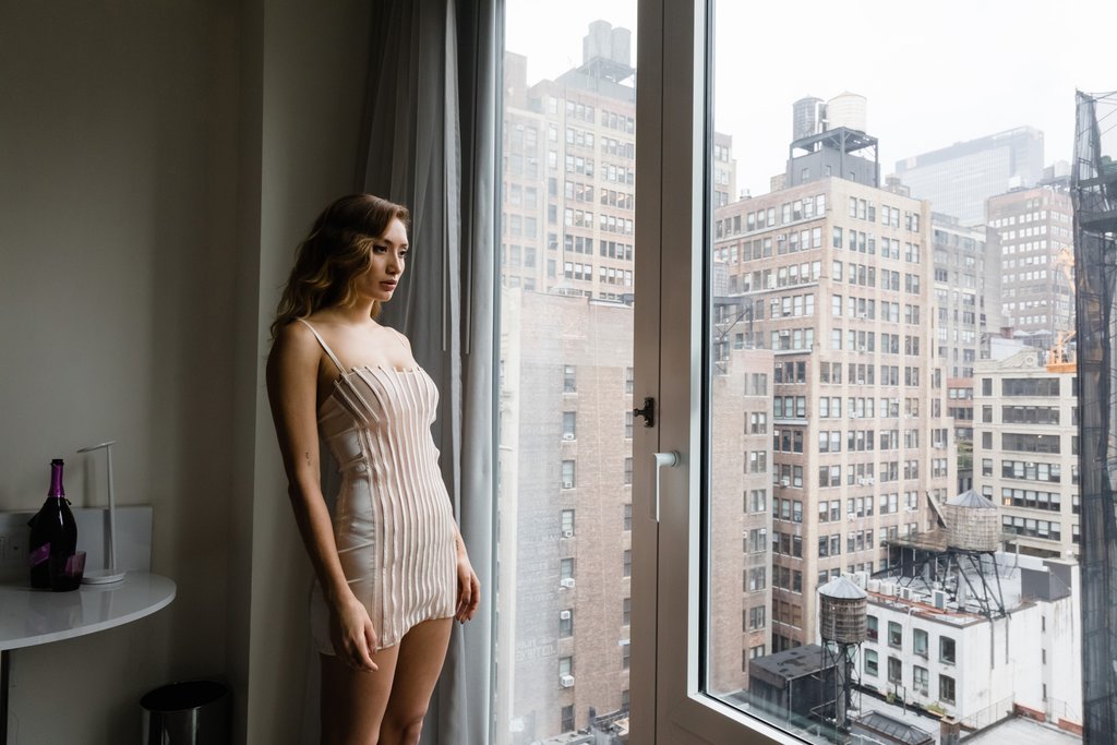 model in lingerie staring out of city high rise window.