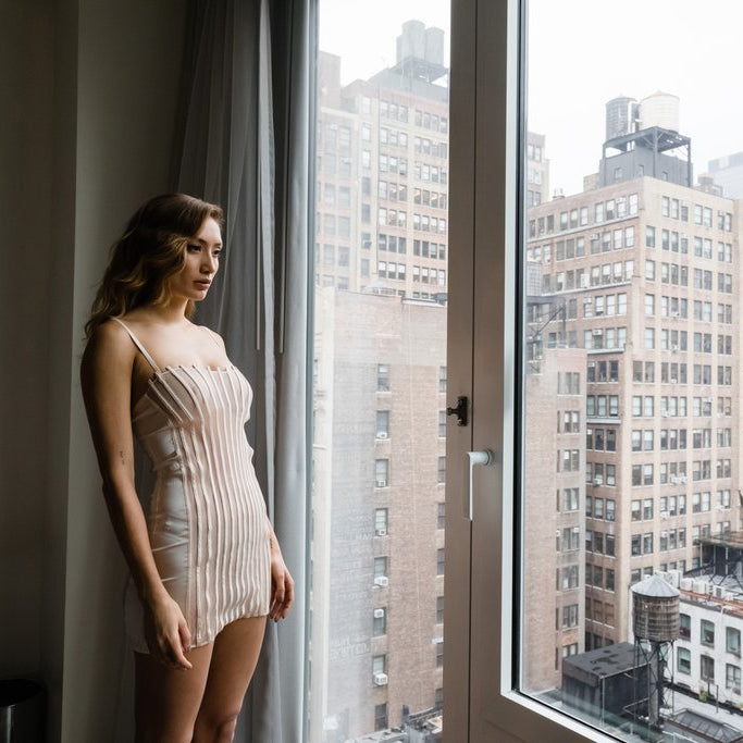 model in lingerie staring out of city high rise window.