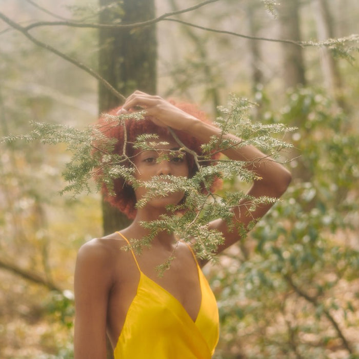 model in yellow slip dress shot through a tree branch. 