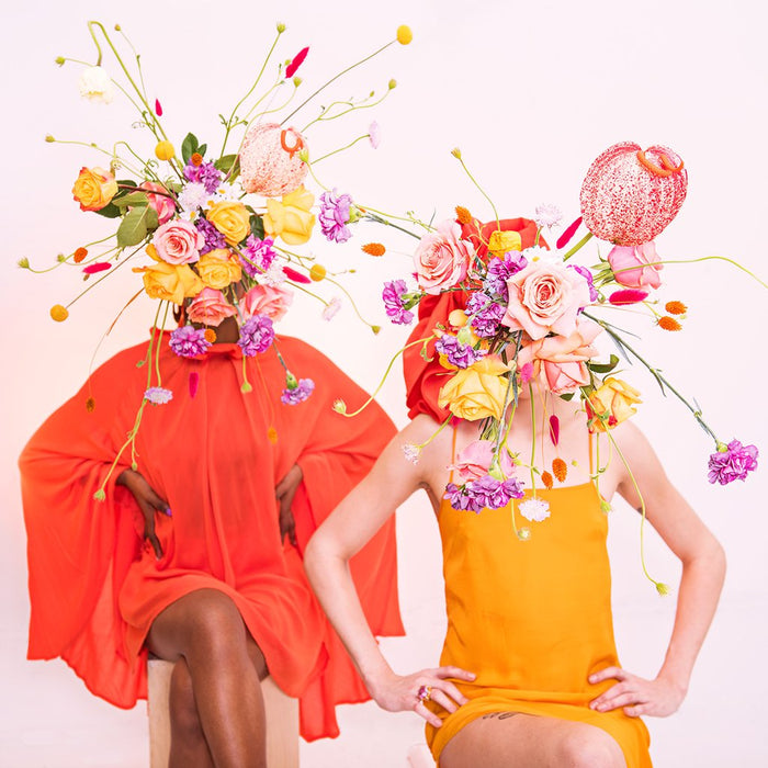 two models seated with tonal dressing and flower bomb bouquets blocking their face.