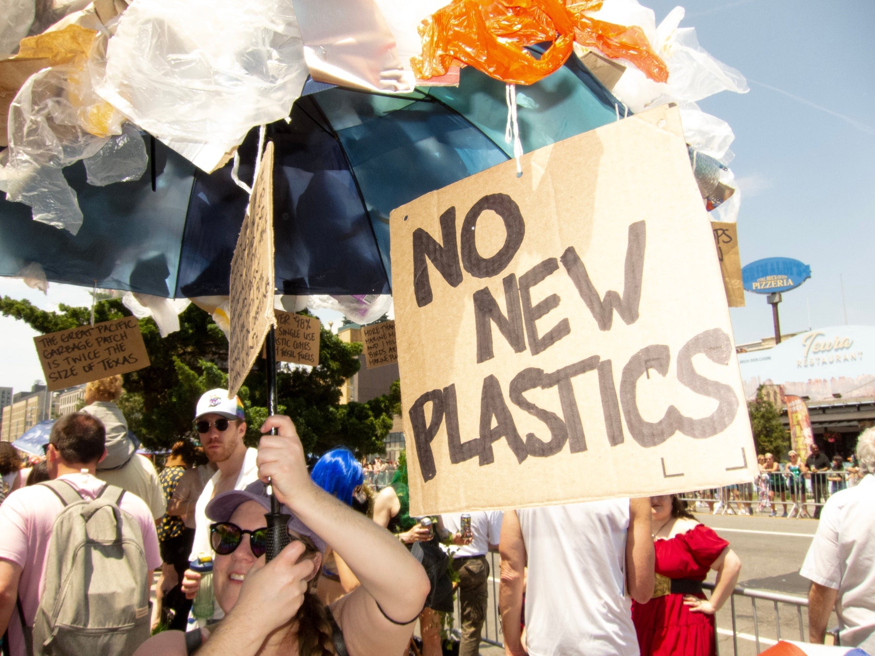 parade goer with protest jellyfish umbrella made of plastic bags - sign hanging reads: no new plastics