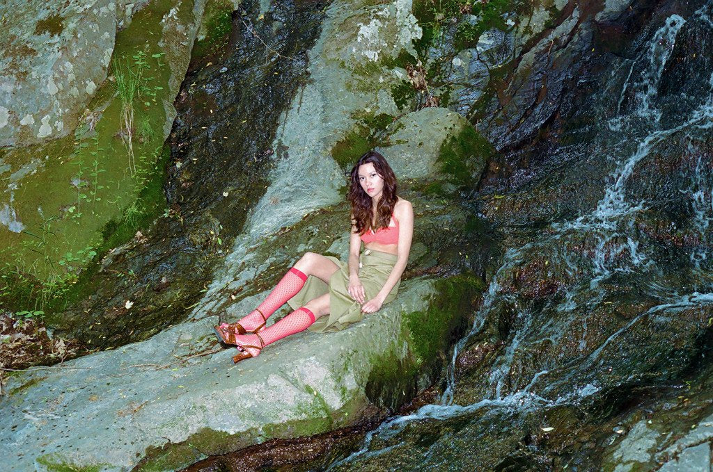 model seated on rocks next to waterfall.