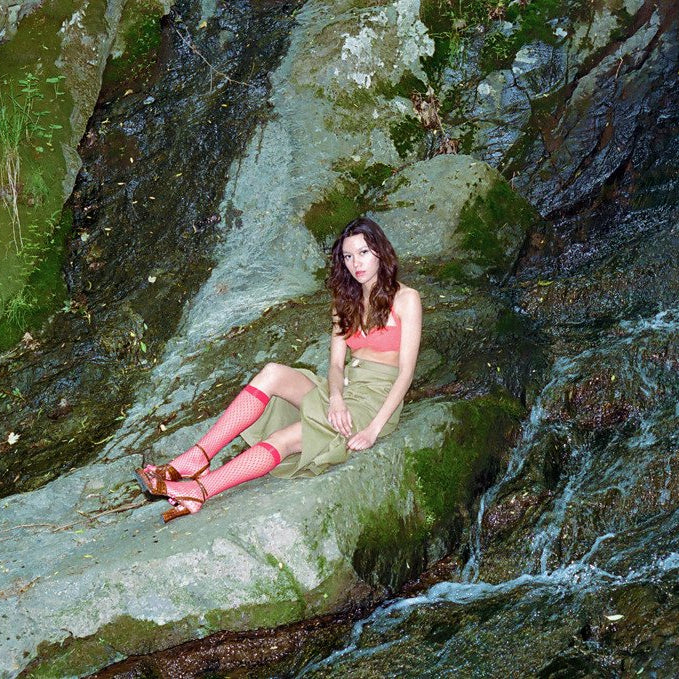 model seated on rocks next to waterfall.