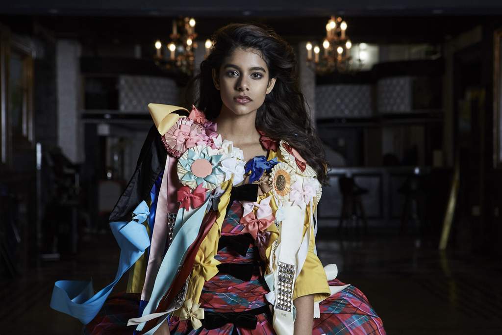 model posing between two chandeliers in voluminous tartan dress covered in bows.