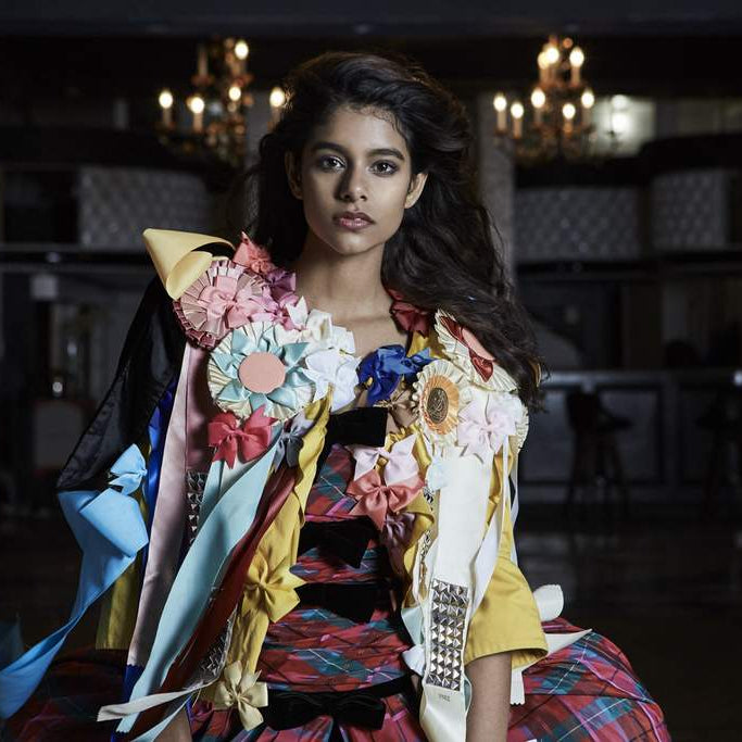model posing between two chandeliers in voluminous tartan dress covered in bows.