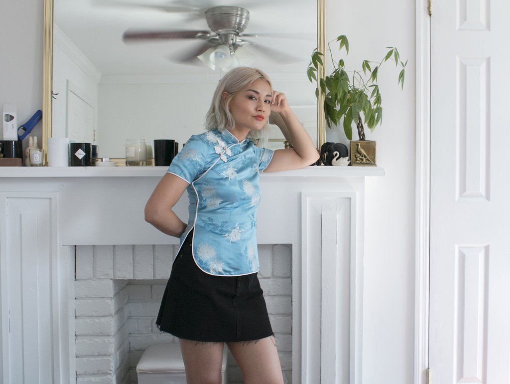 sable wong in embroidered top and mini skirt leaning against mantel.