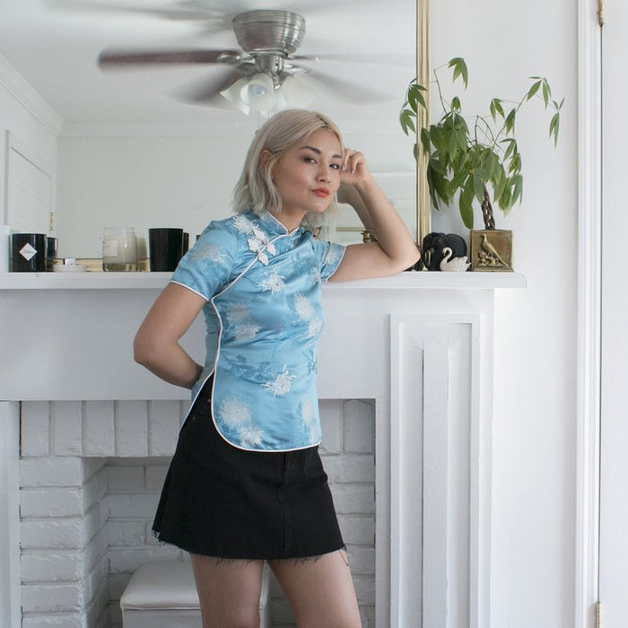 sable wong in embroidered top and mini skirt leaning against mantel.