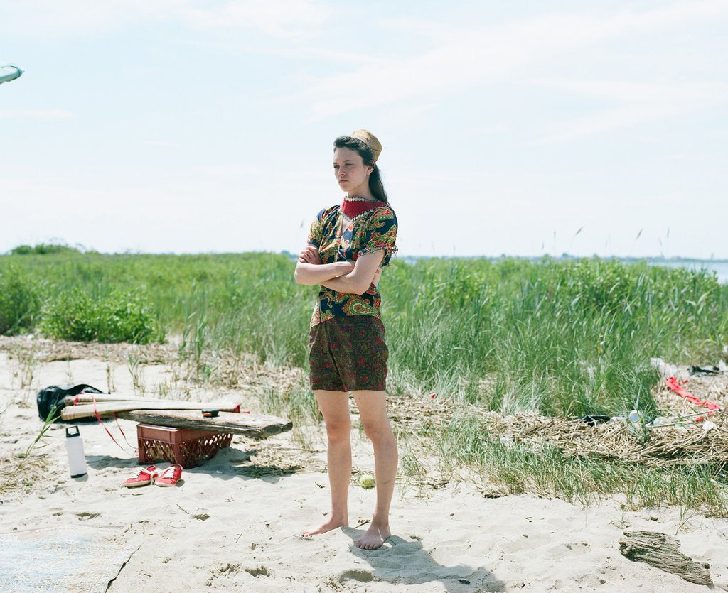 model standing on beach with grass in the background.