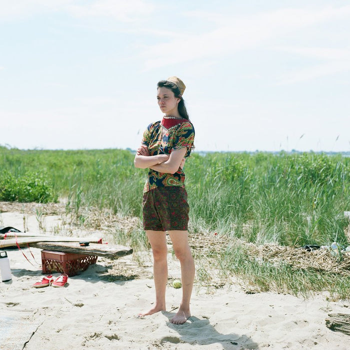 model standing on beach with grass in the background.