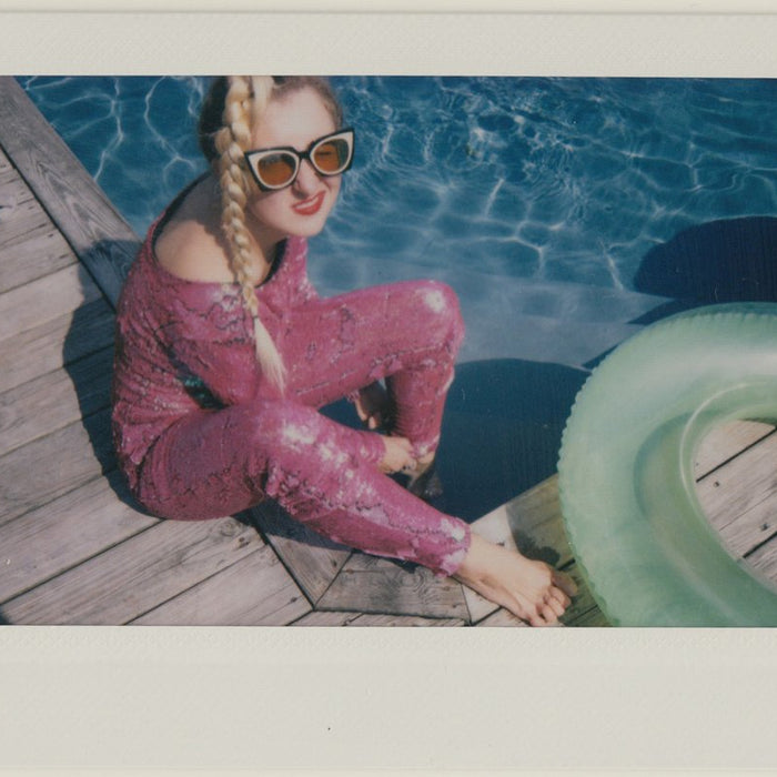 ashley in sequin jumpsuit seated on deck by pool. 