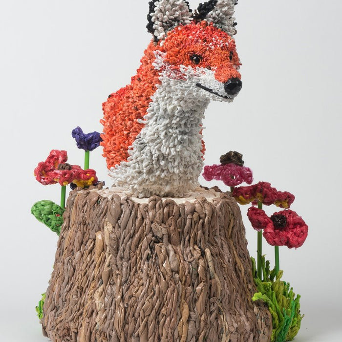 bust of crochet fox on tree stump with flowers.
