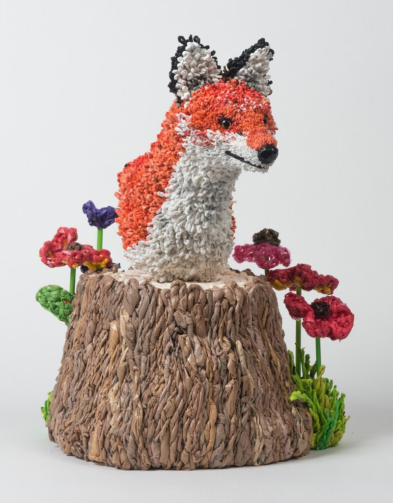 bust of crochet fox on tree stump with flowers. 
