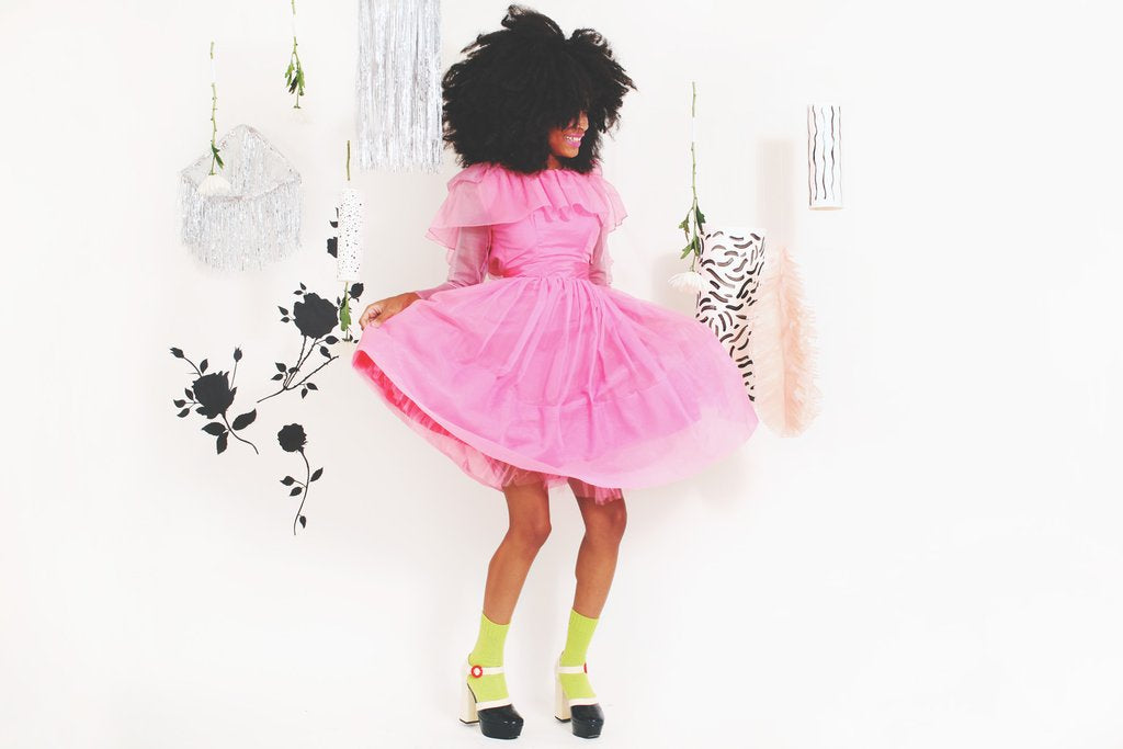 model posing with frilly party dress in front of silver mobiles hanging.