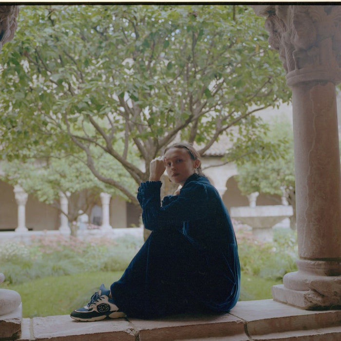 model posing seated with leg up between pillars.