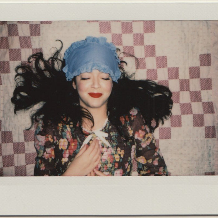 kate in floral dress and denim eye patch laying in bed.