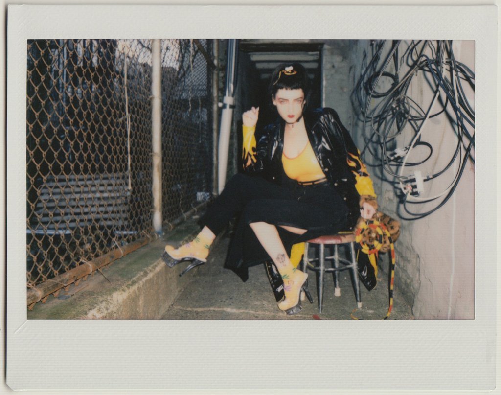 nina seated and posing by chain link fence.