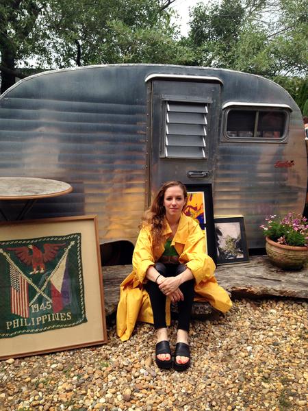 person in a yellow coat taking a seat by a permanent lawn fixture, an old trailer.