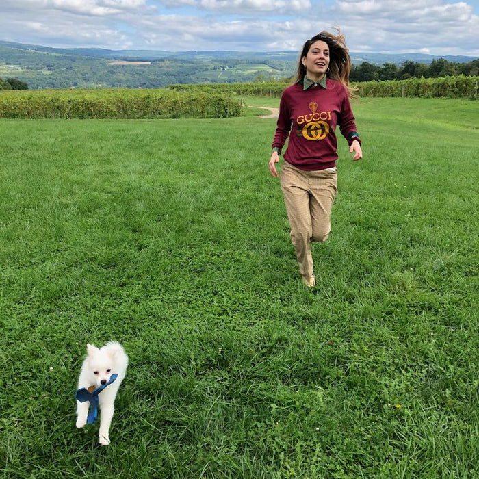 a person running in the fields with a white little dog.