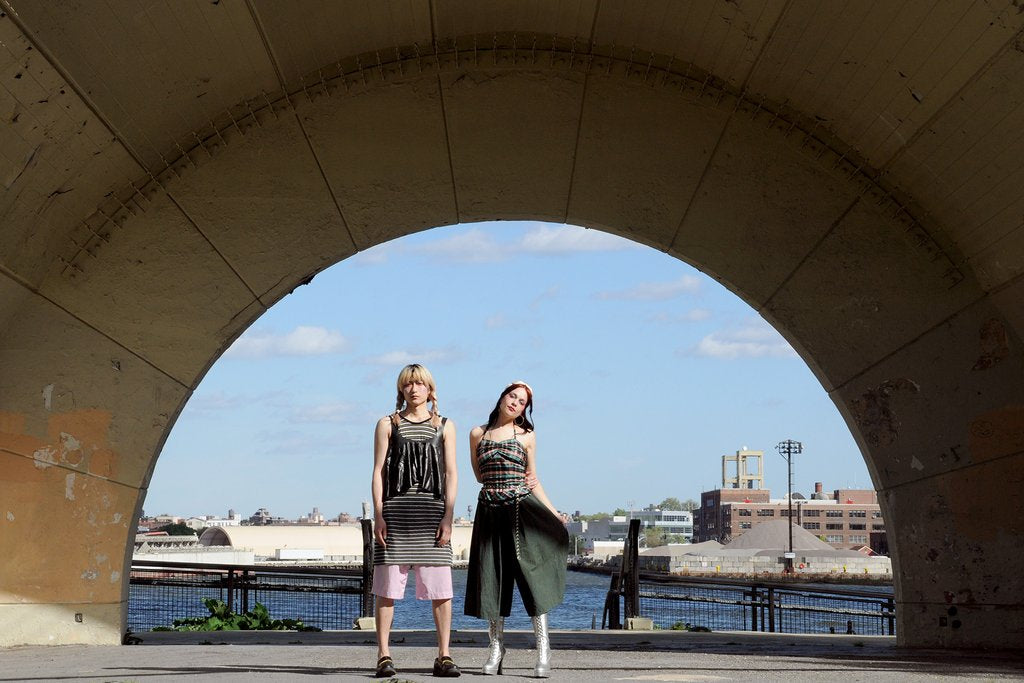 models posing in archway with water in the background.