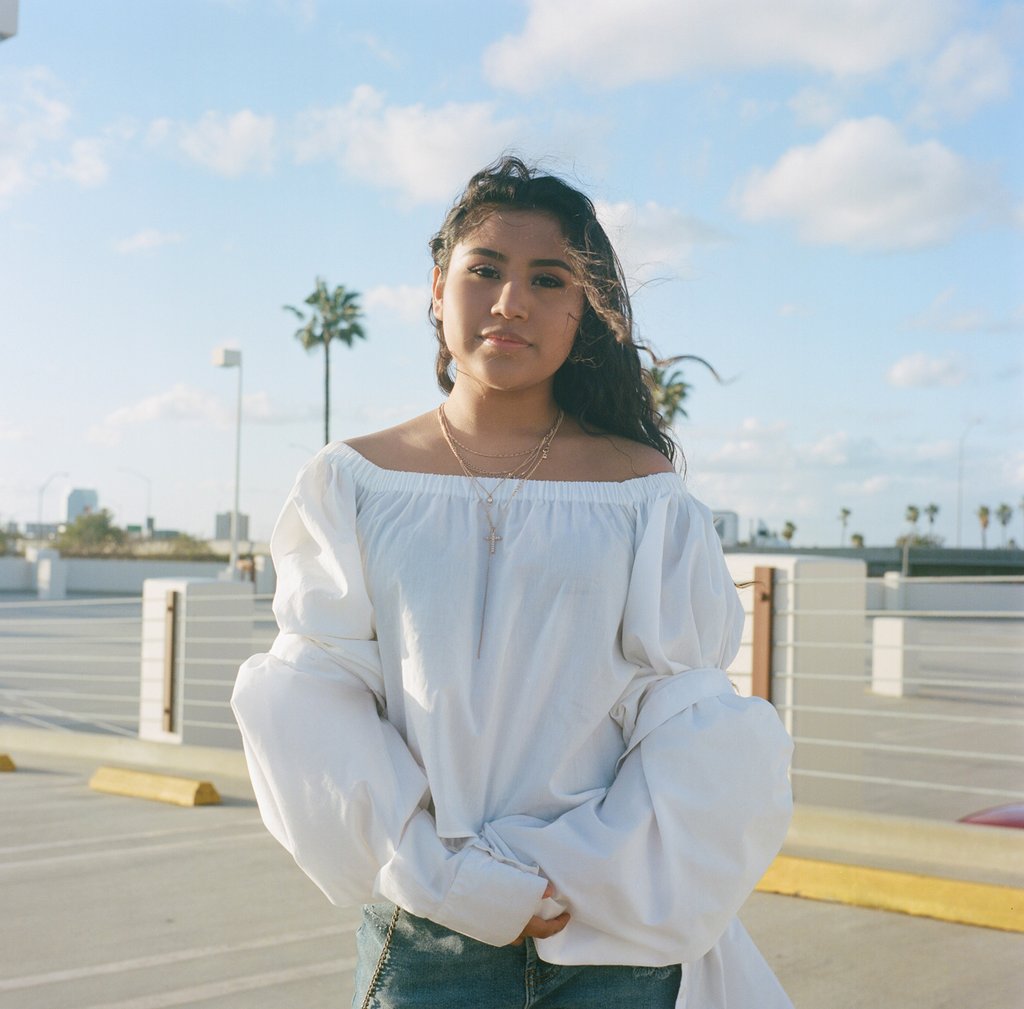 model in parking lot with palm tree behind.