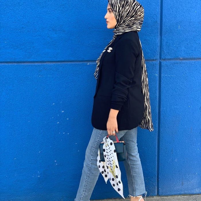 gloria monroy profile in blazer, jeans, and printed head scarf in front of cement wall.