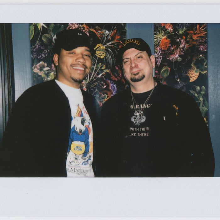 two people wearing hats, smiling side by side with floral wallpaper backdrop - polaroid style.