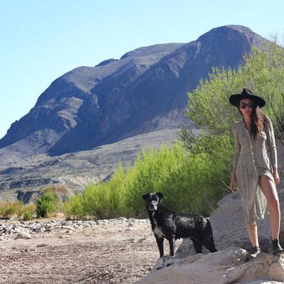 aisha standing on a rock with a black dog, and a mountain in the background.