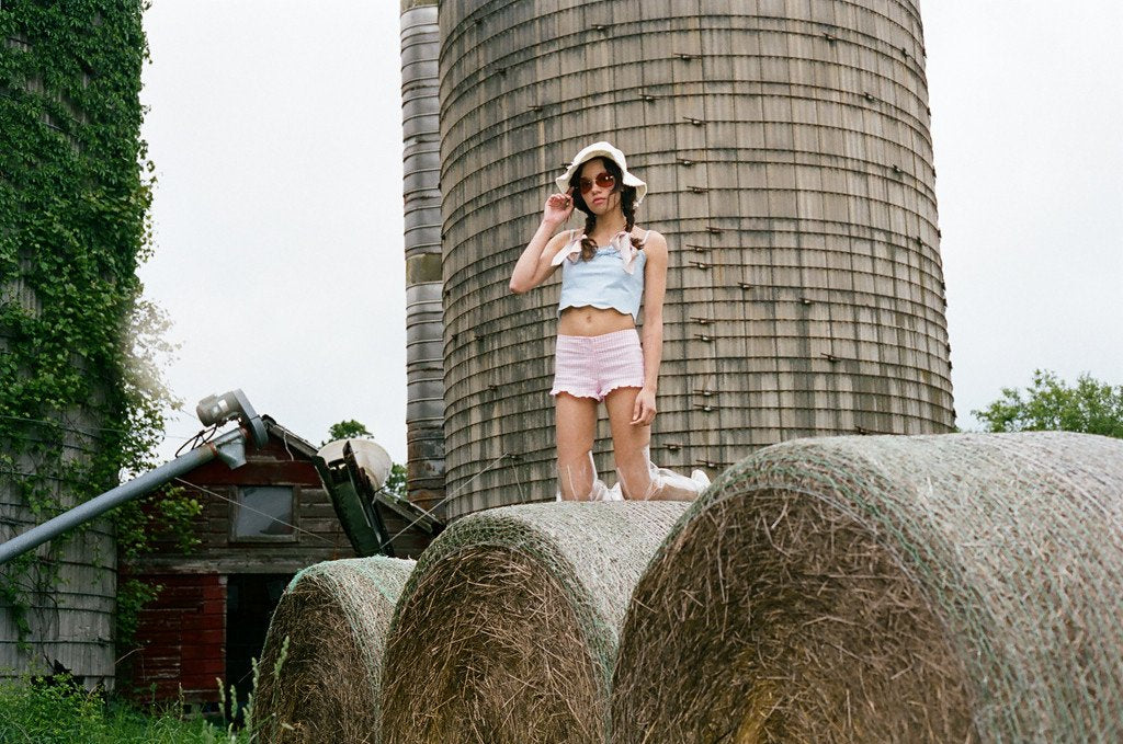 model posing with hand on hat on bales of hay.