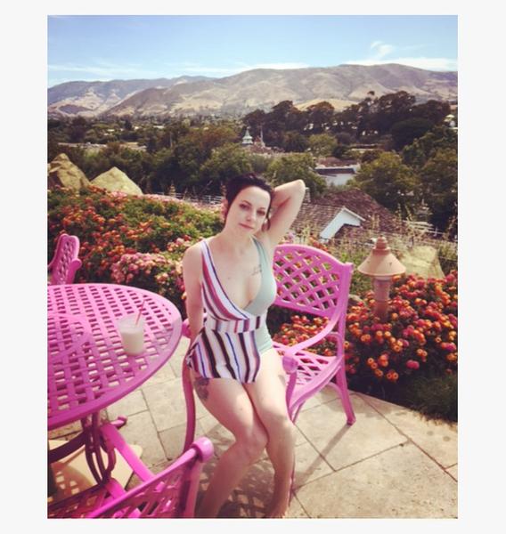 a person sitting on a pink chair, hands behind the head and mountains in the back.