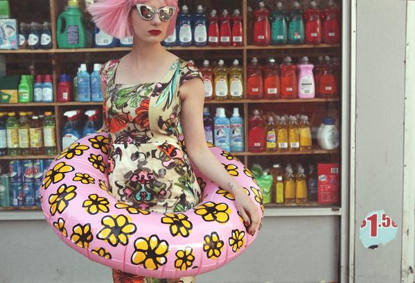 zuzu in gorgeous dress with ring pool float in front of a bodega. 