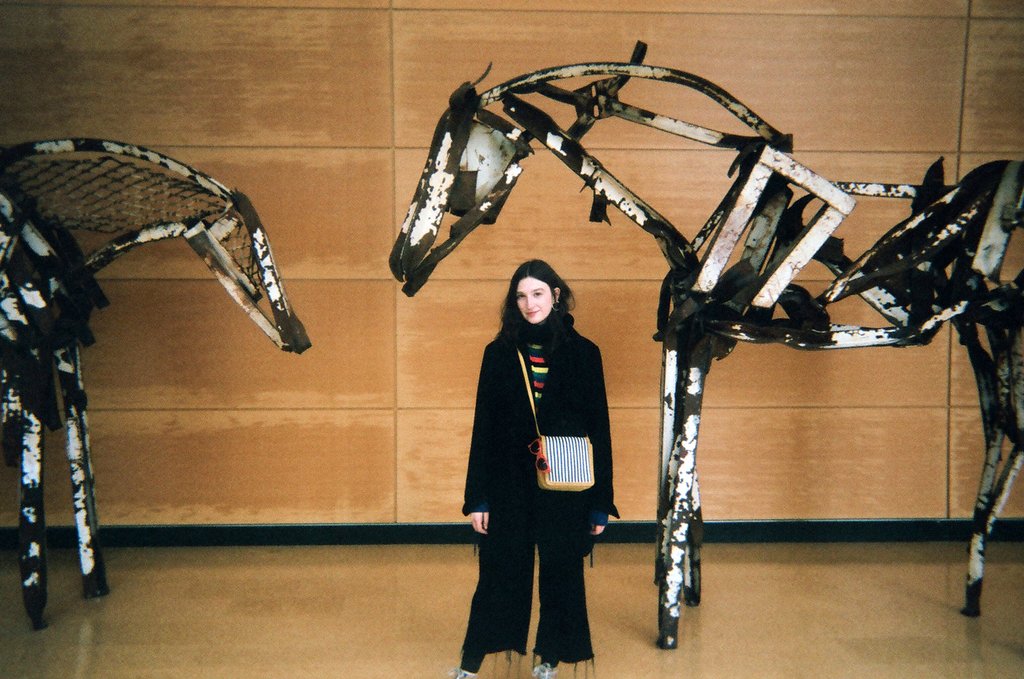 person posing between horses sculptures. 