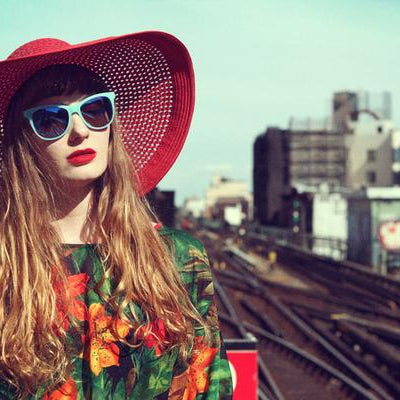 portrait of model in hat and sunglasses on train tracks. 