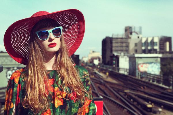portrait of model in hat and sunglasses on train tracks. 