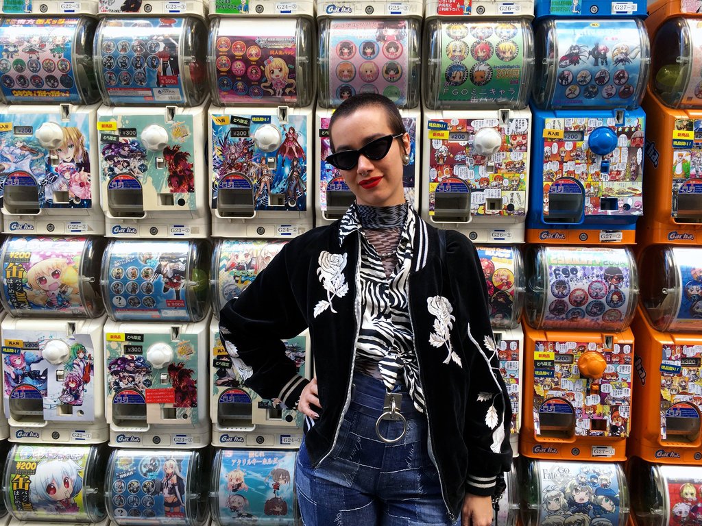 a person wearing sunglasses posing in front of a wall of toy vending machines.