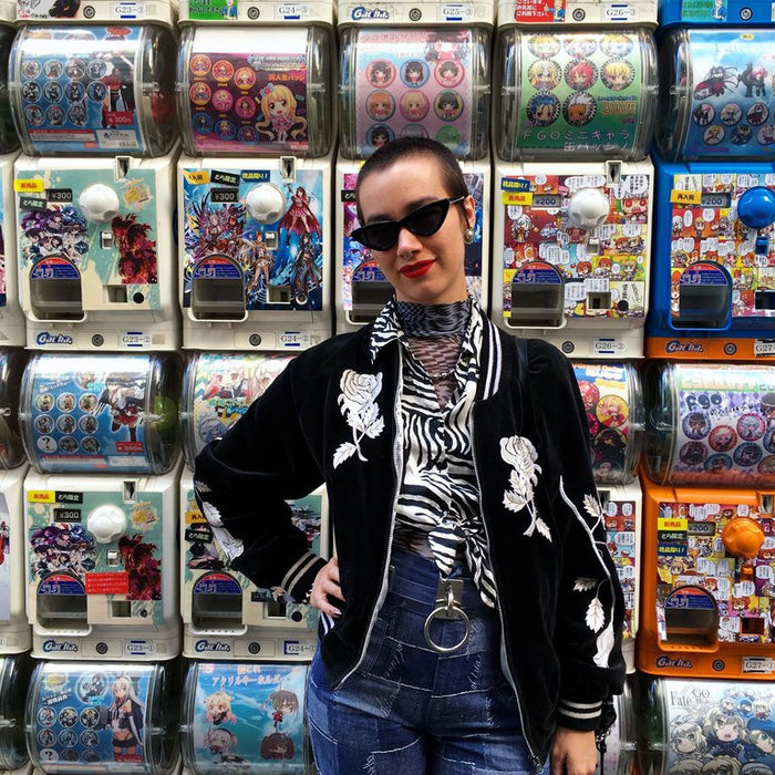 a person wearing sunglasses posing in front of a wall of toy vending machines.