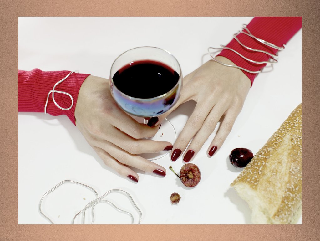 still life of hands in bracelets with glass of wine and cherries. 
