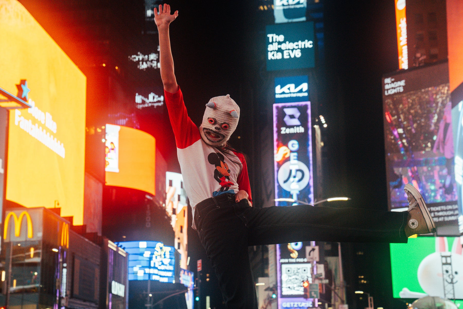 katrina in vejigante mask and mickey mouse t-shirt in times square with blurred neon signage in background.