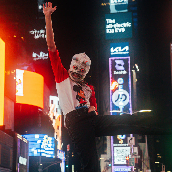 katrina in vejigante mask and mickey mouse t-shirt in times square with blurred neon signage in background.