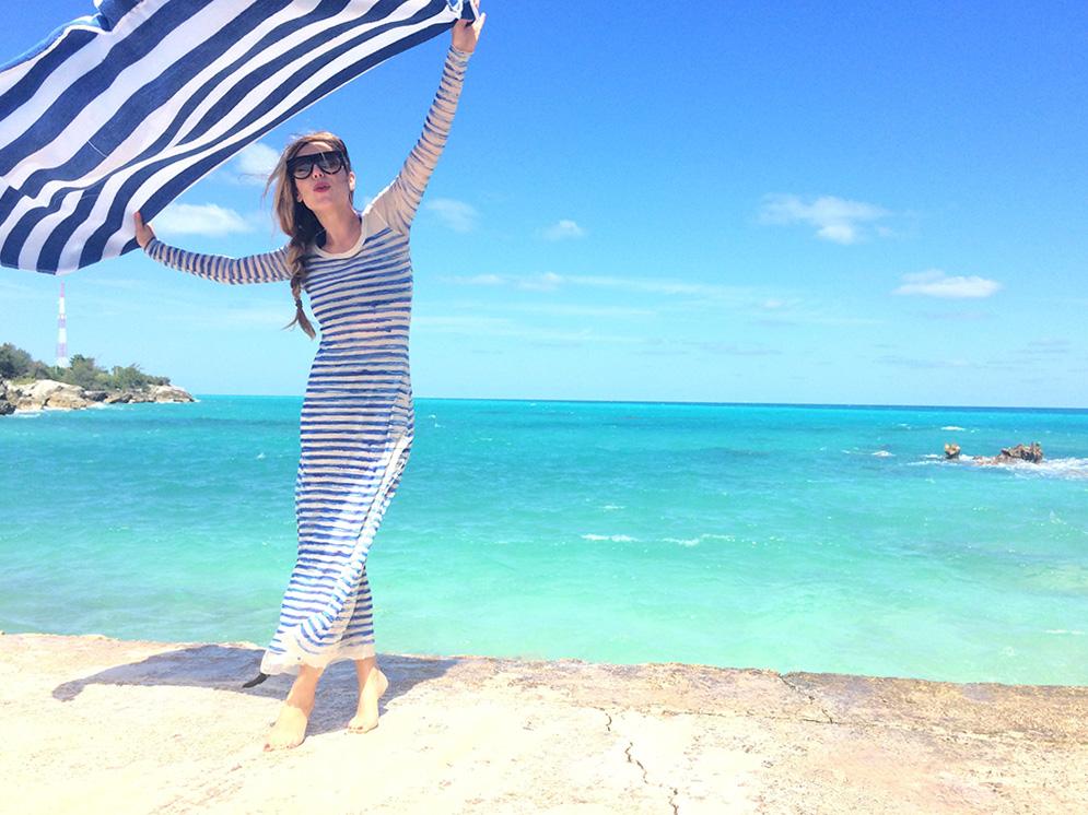 person holding striped towel with beach view in the background. 