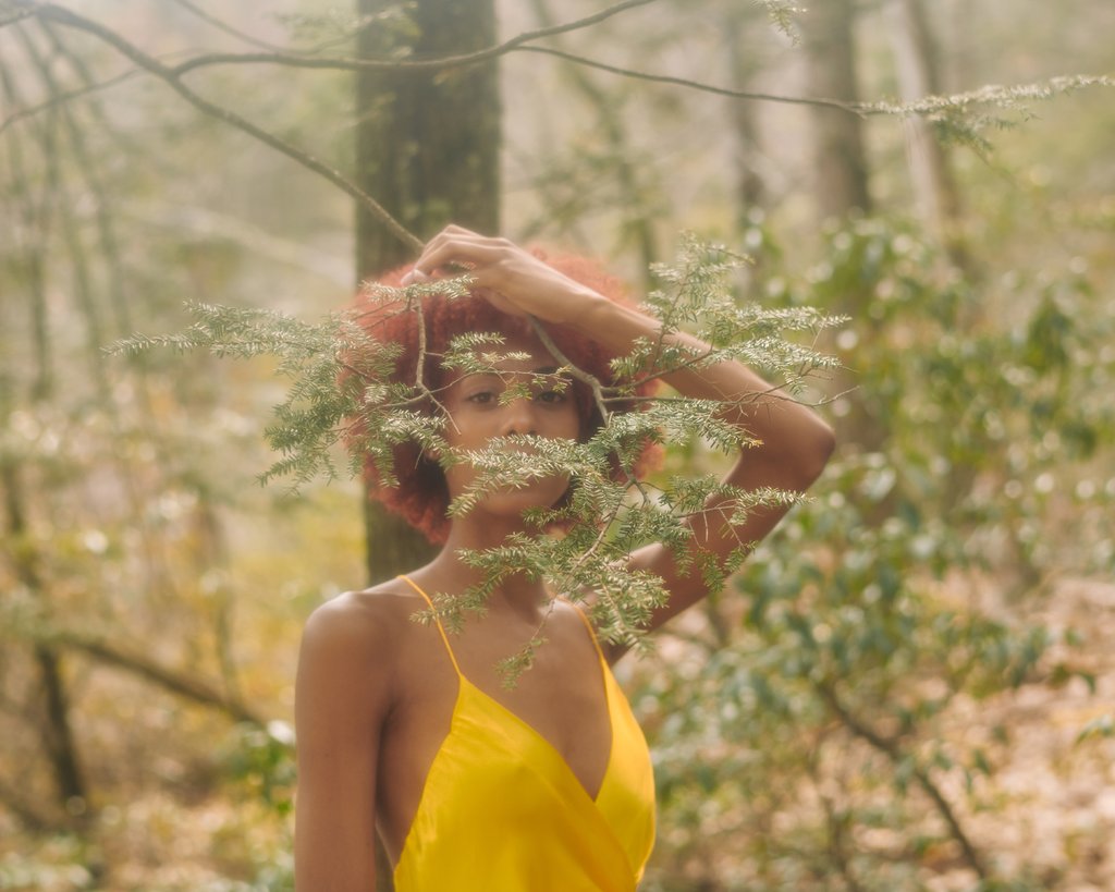 model in yellow slip dress shot through a tree branch. 