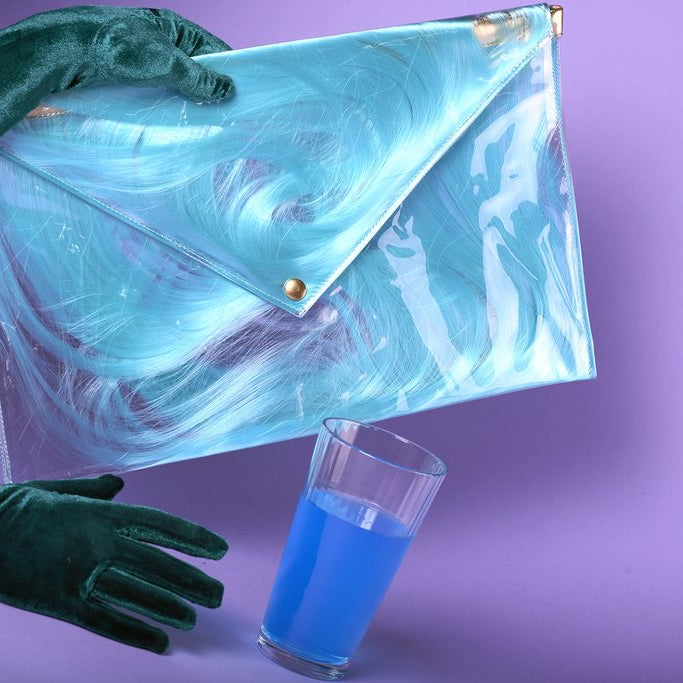 conceptual still life featuring spilling glass of liquid, clear clutch with hair and velvet gloves. 